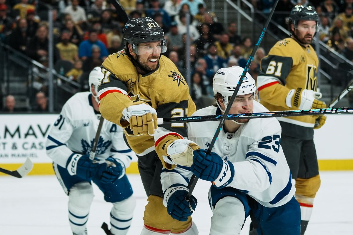 Vegas Golden Knights defenseman Shea Theodore (27)  and Maple Leafs left wing Matthew Knies (23) reach for the puck during second period of NHL game against Toronto Maple Leafs on Thursday Jan. 15, 2026 at T-Mobile Arena in Las Vegas.