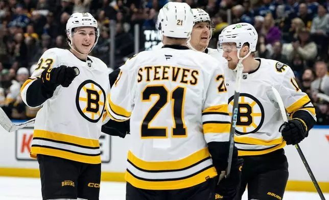 Boston Bruins' Fraser Minten, left, celebrates after his goal against the Vancouver Canucks with Alex Steeves (21), Hampus Lindholm (27), and Casey Mittelstadt (11) during the first period of an NHL hockey game in Vancouver, British Columbia, Saturday, Jan. 3, 2026. (Ethan Cairns/The Canadian Press via AP)