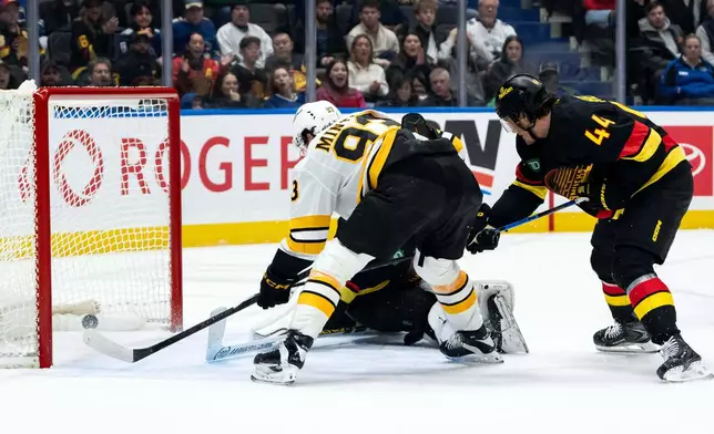 Boston Bruins' Fraser Minten (93) scores on Vancouver Canucks goaltender Kevin Lankinen (32) as Kiefer Sherwood (44) defends during overtime in an NHL hockey game in Vancouver, British Columbia, on Saturday, Jan. 3, 2026. (Ethan Cairns/The Canadian Press via AP)
