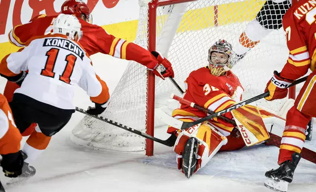Philadelphia Flyers' Travis Konecny, left, scores on Calgary Flames goalie Dustin Wolf during second period NHL hockey action in Calgary on Wednesday, Dec. 31, 2025. (Jeff McIntosh/The Canadian Press via AP)