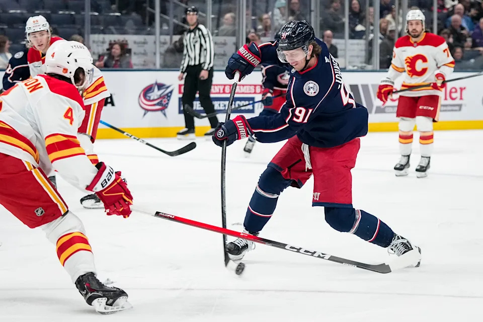 Blue Jackets center Kent Johnson shoots past Flames defenseman Rasmus Andersson.