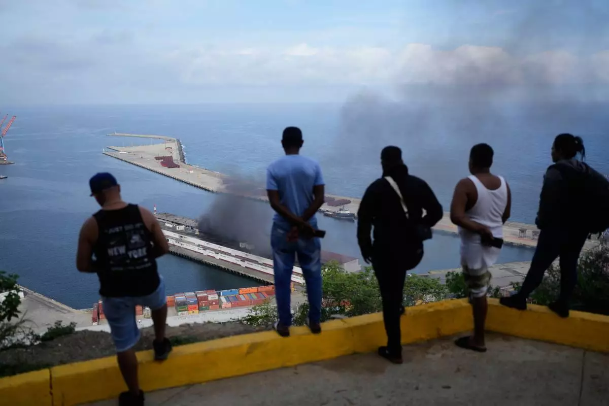 Men watch smoke rising from a dock after explosions were heard at La Guaira port, Venezuela, Saturday, Jan. 3, 2026. (AP Photo/Matias Delacroix)