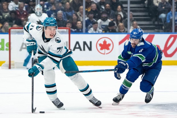 San Jose Sharks' Macklin Celebrini (71) and Vancouver Canucks' Conor Garland (8) vie for the puck during the first period of an NHL hockey game in Vancouver, British Columbia, Saturday, Dec. 27, 2025. (Ethan Cairns/The Canadian Press via AP)