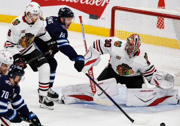 Jets center Jonathan Toews (19) reaches for the puck between the Blackhawks defenseman Sam Rinzel, left, and goalie Spencer Knight during second-period Oct. 30, 2025, in Winnipeg, Manitoba. (John Woods/The Canadian Press via AP)