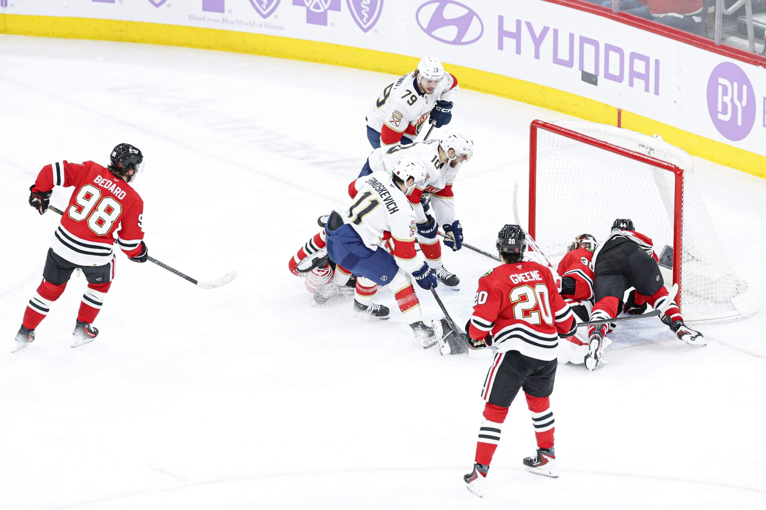 Three Panthers players get the puck in the Blackhawks' net with Connor Bedard and Ryan Greene skating closer.