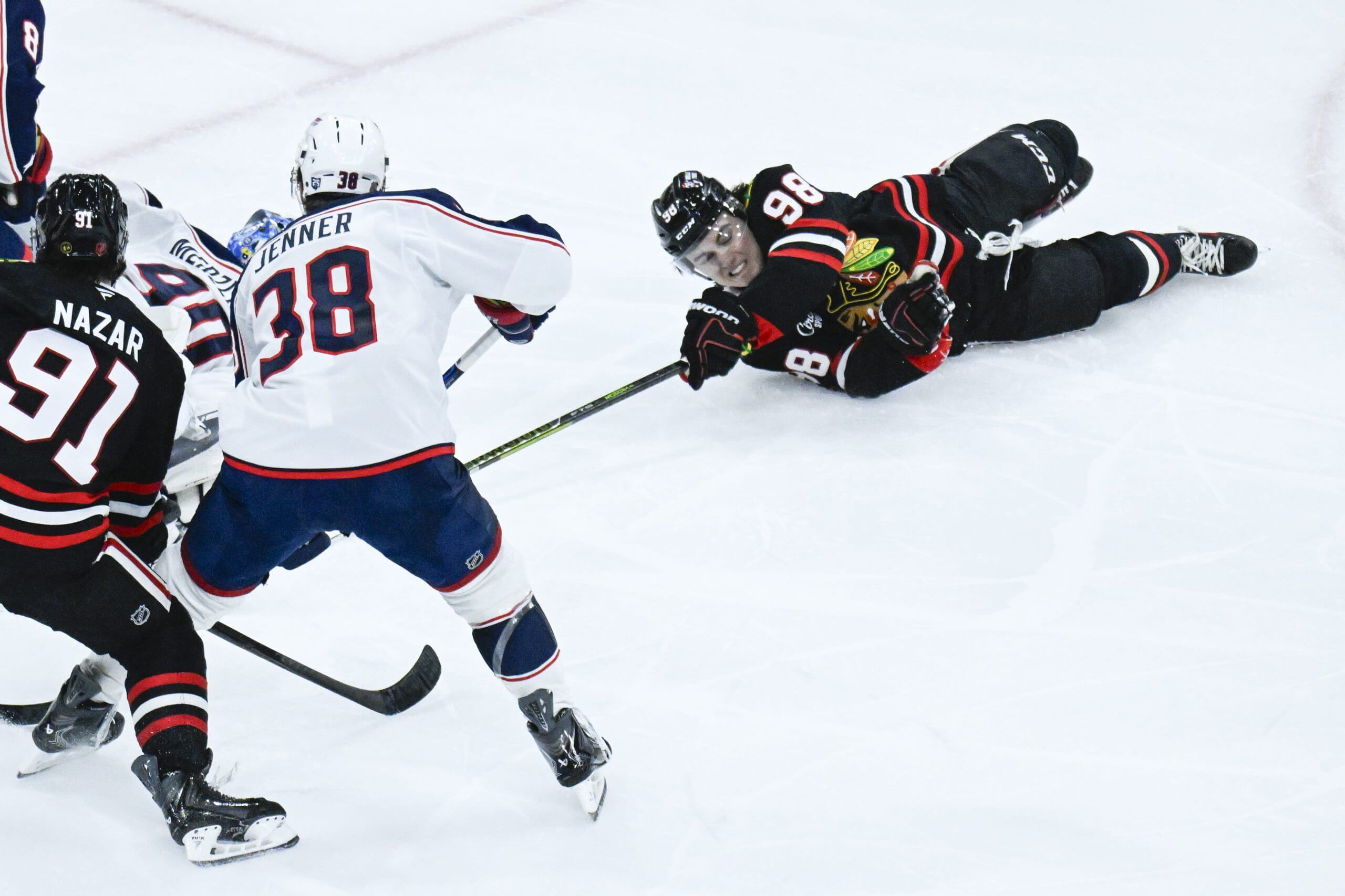 Blackhawks center Connor Bedard, right, wearing No. 98 on his jersey, dives on the ice for a puck with his stick extended against Blue Jackets goaltender Elvis Merzlikins, left, and center Boone Jenner.