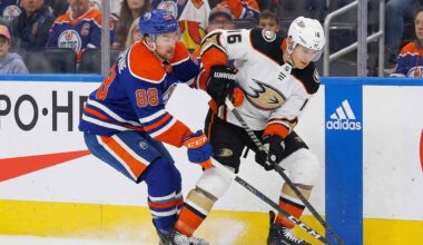 Edmonton Oilers forward Andrew Mangiapane (88) in a blue home jersey and Anaheim Ducks center Ryan Strome (16) in a white away jersey battle for possession of the puck along the rink boards during an NHL game.