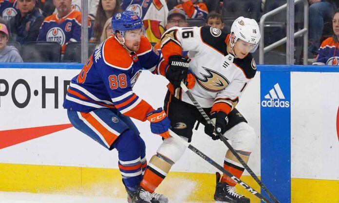 Edmonton Oilers forward Andrew Mangiapane (88) in a blue home jersey and Anaheim Ducks center Ryan Strome (16) in a white away jersey battle for possession of the puck along the rink boards during an NHL game.