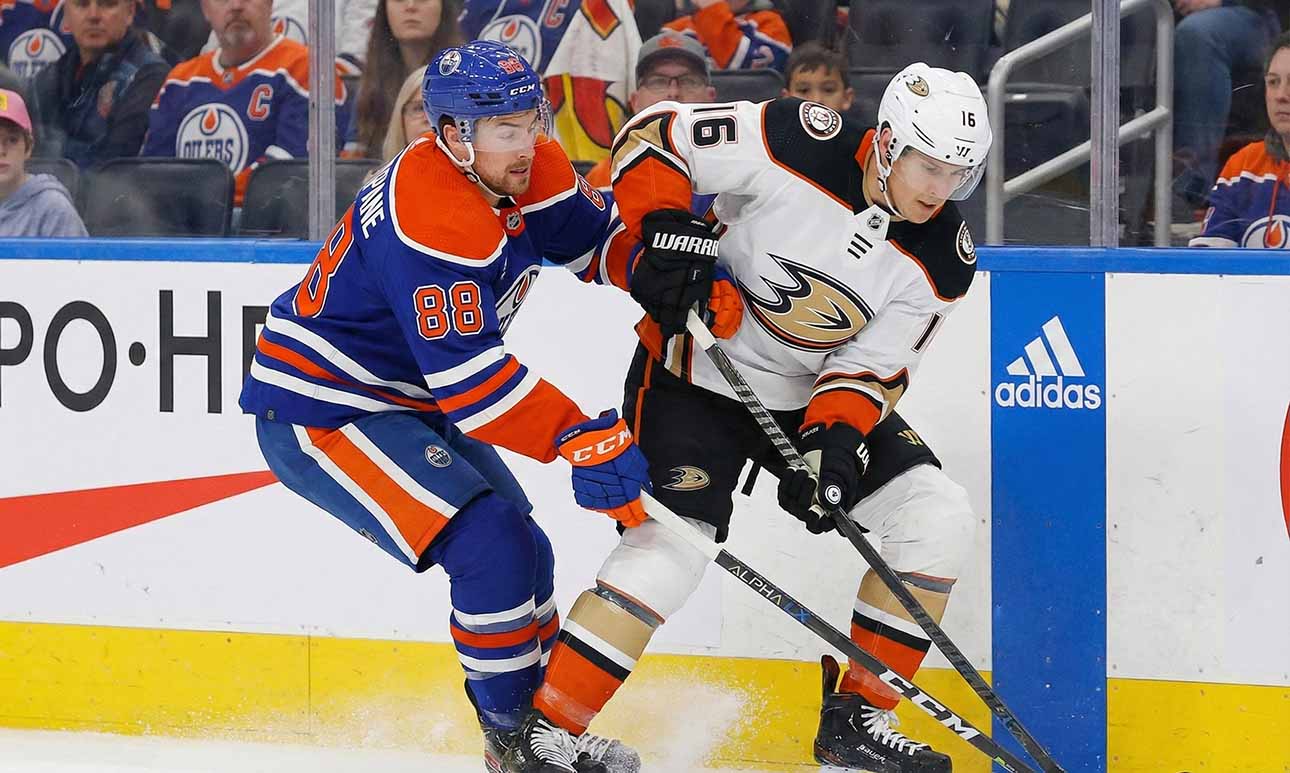 Edmonton Oilers forward Andrew Mangiapane (88) in a blue home jersey and Anaheim Ducks center Ryan Strome (16) in a white away jersey battle for possession of the puck along the rink boards during an NHL game.