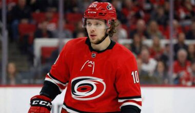 A close-up photograph of NHL forward Artemi Panarin wearing a red Carolina Hurricanes home jersey with the number 10 and a matching red helmet, looking towards the left side of the rink during a game.