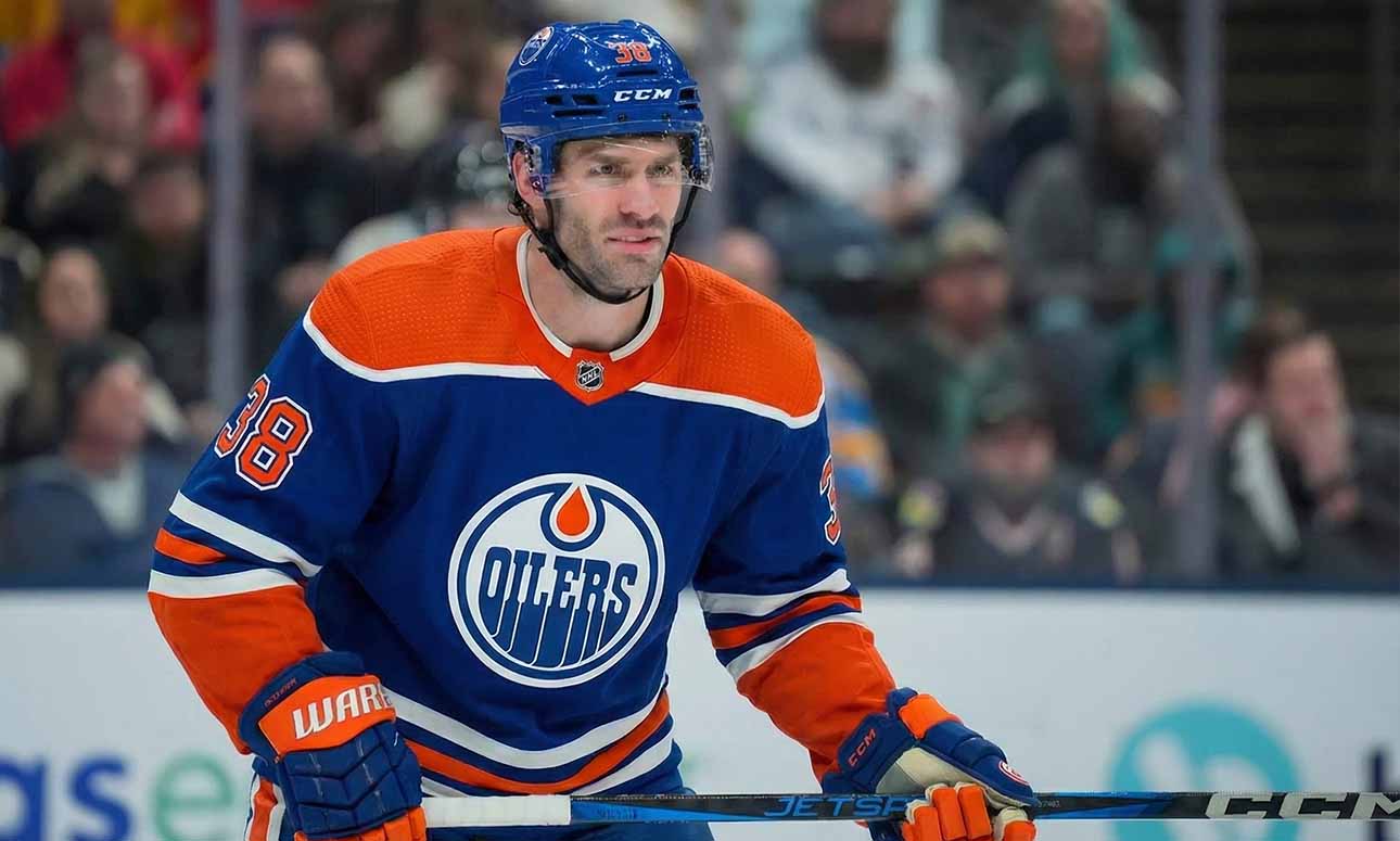 Edmonton Oilers forward Boone Jenner, wearing the blue #38 home jersey, stands on the ice holding his stick during a game, looking towards the play.