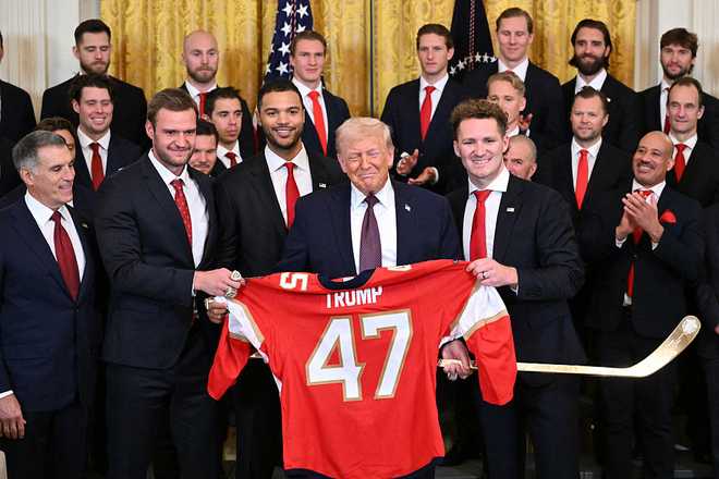 US President Donald Trump poses with a team shirt and a golden hockey stick presented to him by players of the Florida Panthers of the National Hockey League, winners of the 2025 Stanley Cup, during a congratulatory ceremony in the East Room of the White House in Washington, DC on January 15, 2026. (Photo by Mandel NGAN / AFP via Getty Images)
