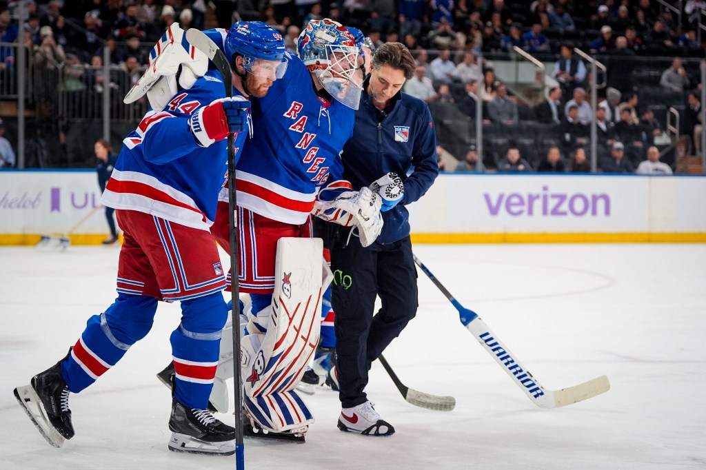 New York Rangers goalie Igor Shesterkin is helped off the ice by a teammate and trainer.