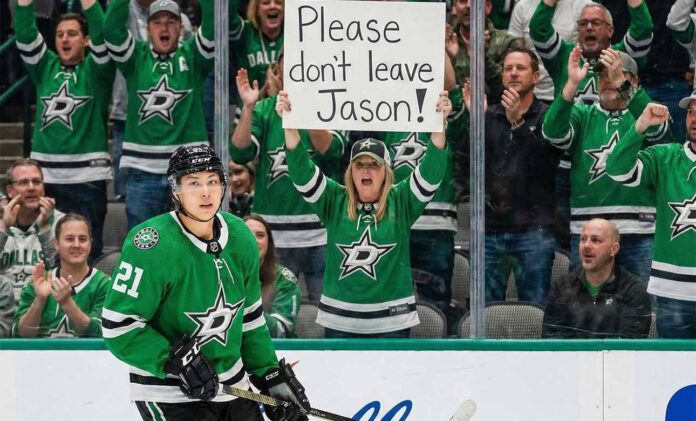 Dallas Stars forward Jason Robertson skates on the ice while a female fan behind the glass holds a handwritten sign that reads, 'Please don't leave Jason!'.