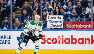 Jason Robertson of the Dallas Stars in his white away uniform skates on the ice during an NHL game against the Toronto Maple Leafs, with fans visible in the stands behind the glass.