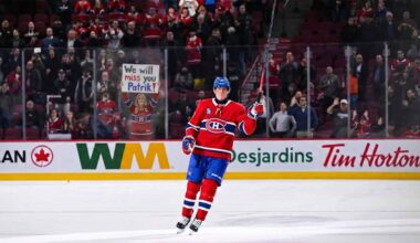Montreal Canadiens forward Patrik Laine skates on the ice, saluting the crowd with his stick raised. Behind the rink glass, a female fan in a Habs jersey holds a handmade sign reading "We will miss you Patrik!".