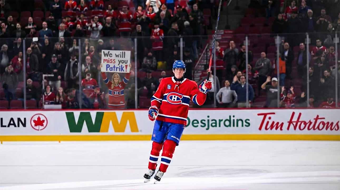 Montreal Canadiens forward Patrik Laine skates on the ice, saluting the crowd with his stick raised. Behind the rink glass, a female fan in a Habs jersey holds a handmade sign reading "We will miss you Patrik!".