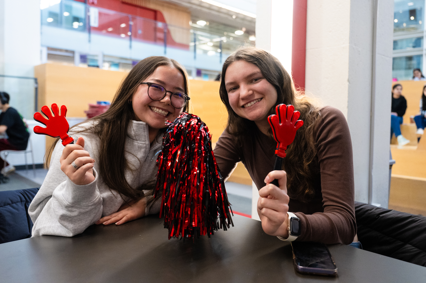 Two students hold red hand shaped clappers while sitting at a table in Curry Student Center. 