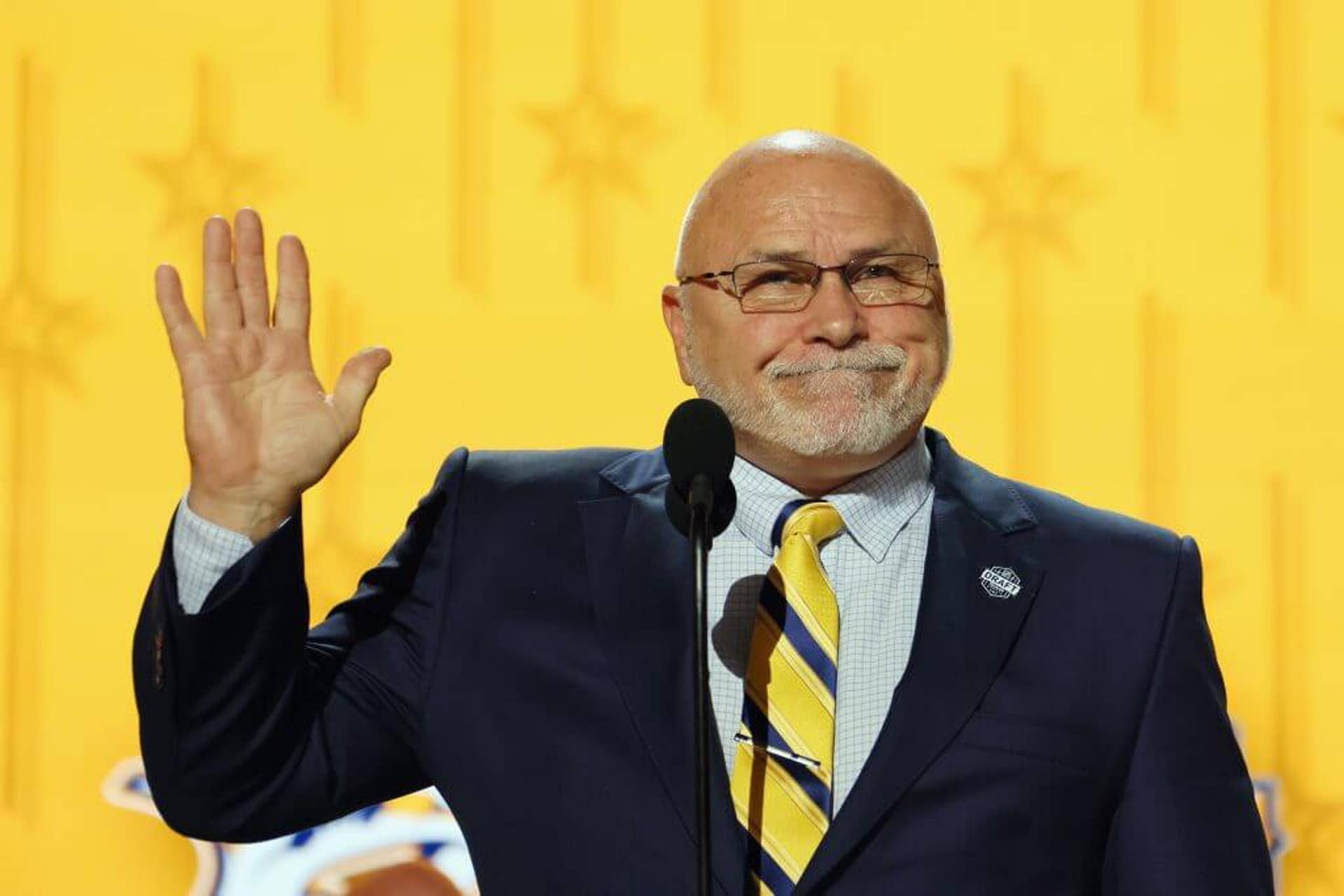 Barry Trotz holds up his right hand on stage to acknowledge the crowd at the 2023 NHL Draft.