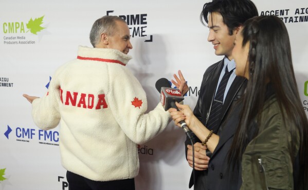 Hudson Williams, of the TV series "Heated Rivalry," center, presents Canadian Prime Minister Mark Carney with a fleece from the show on the red carpet at the Prime Time screen and media industry conference gala in Ottawa, Ontario, Thursday, Jan. 29, 2026. (Patrick Doyle/The Canadian Press via AP)