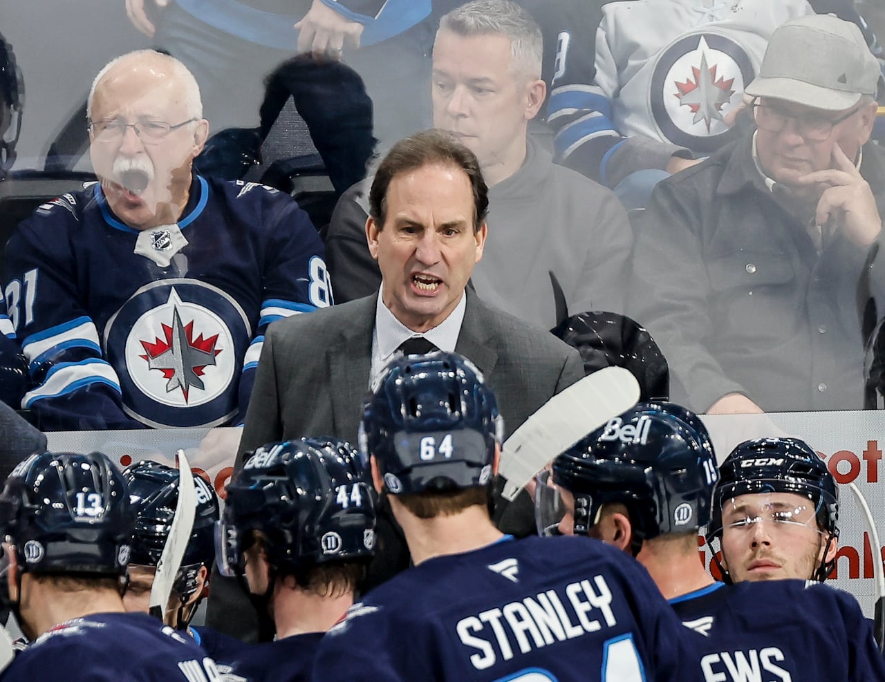 A man in a suit scowls behind the Winnipeg Jets bench.