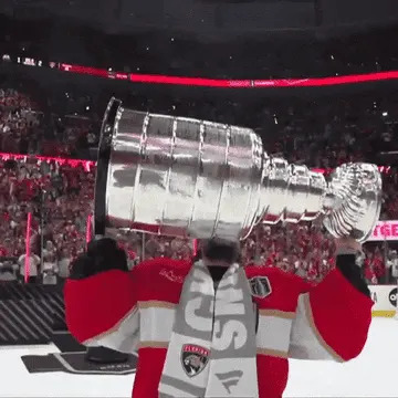 A hockey player raises the Stanley Cup above their head and smiles as they skate on the ice