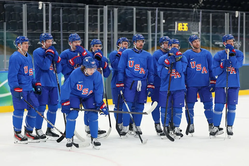 Ice hockey players in Team USA uniforms during practice session on the ice rink several players standing together and one bending forward Gregory Shamus/Getty