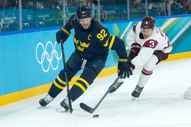 Sweden's Gabriel Landeskog (92) is challenged by Latvia's Alberts Smits (3) during a men's ice hockey qualification playoff game between Sweden and Latvia at the 2026 Winter Olympics, in Milan, Italy, on Tuesday, Feb. 17, 2026. (AP Photo/Petr David Josek)