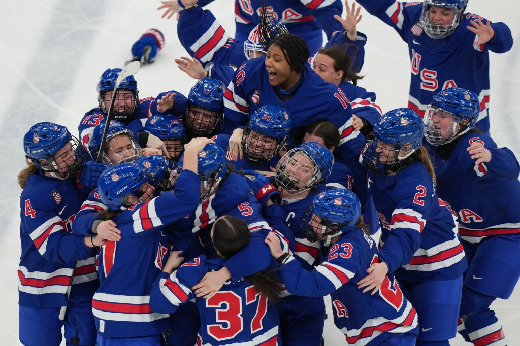 United States players surround Megan Keller (5) after she scored the winning goal in overtime to beat Canada in the women's ice hockey gold medal game at the 2026 Winter Olympics, in Milan, Italy, Feb. 19, 2026.