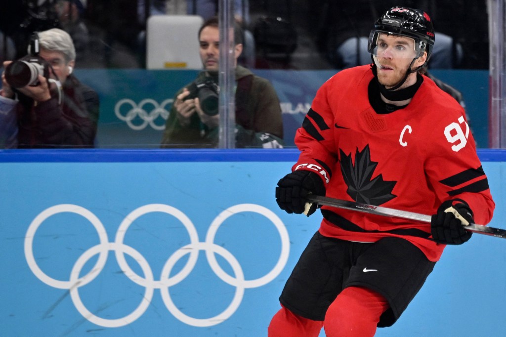 Connor McDavid in his red Canada jersey with number 97 and C, looking right on the ice with the Olympic rings in the background.