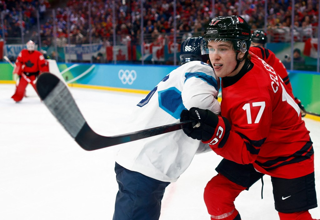 Macklin Celebrini wearing a red Team Canada jersey, with another player in a white jersey in an ice hockey game.