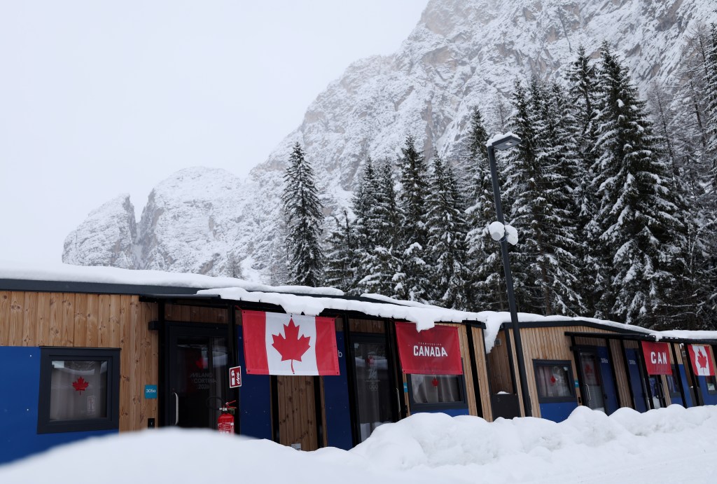 The Canadian team village for the Milano Cortina 2026 Winter Olympics, with snow-covered mountains and trees in the background.