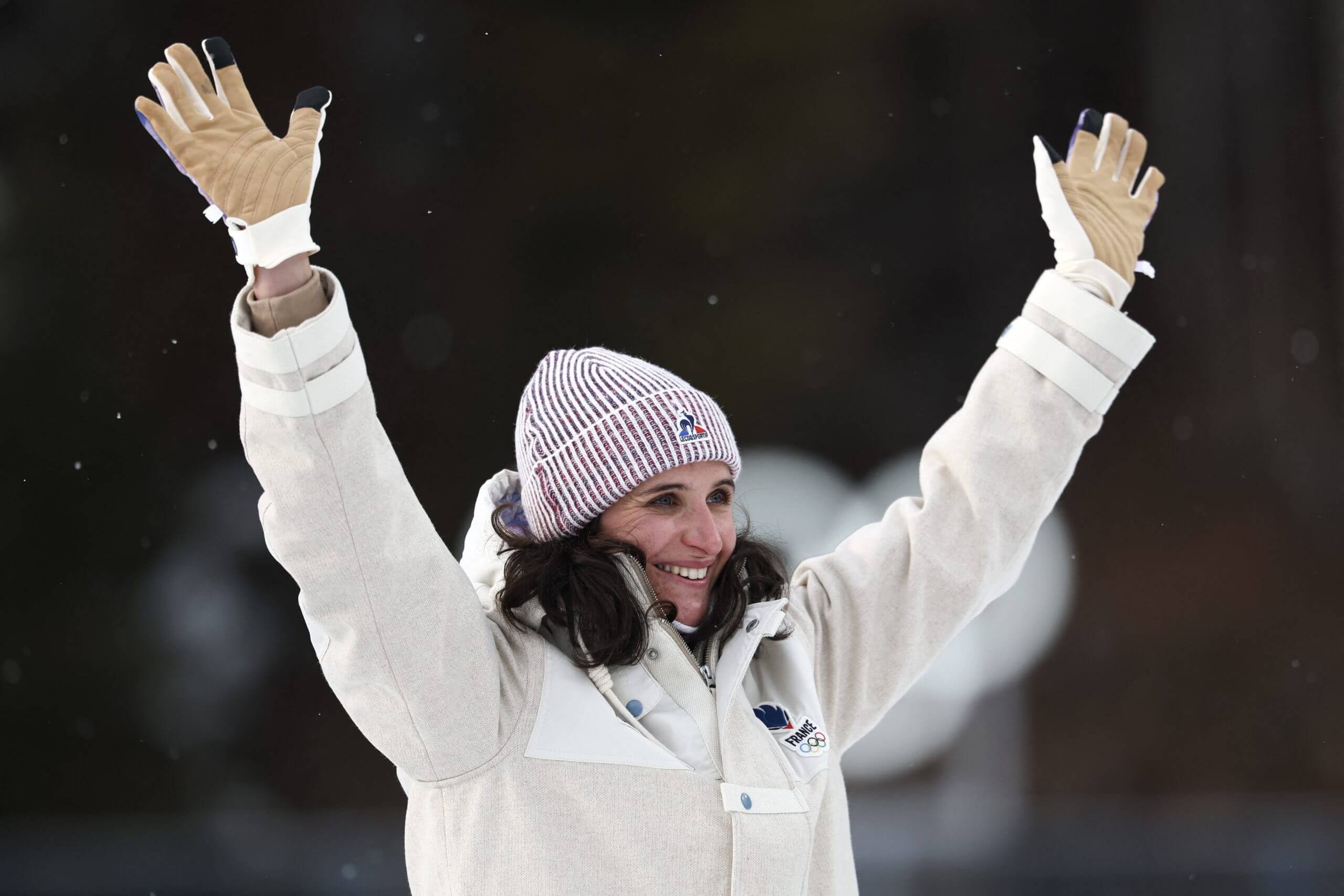 France's Julia Simon poses on the podium of the women's biathlon 15km individual event, her arms outstretched and a smile on her face.