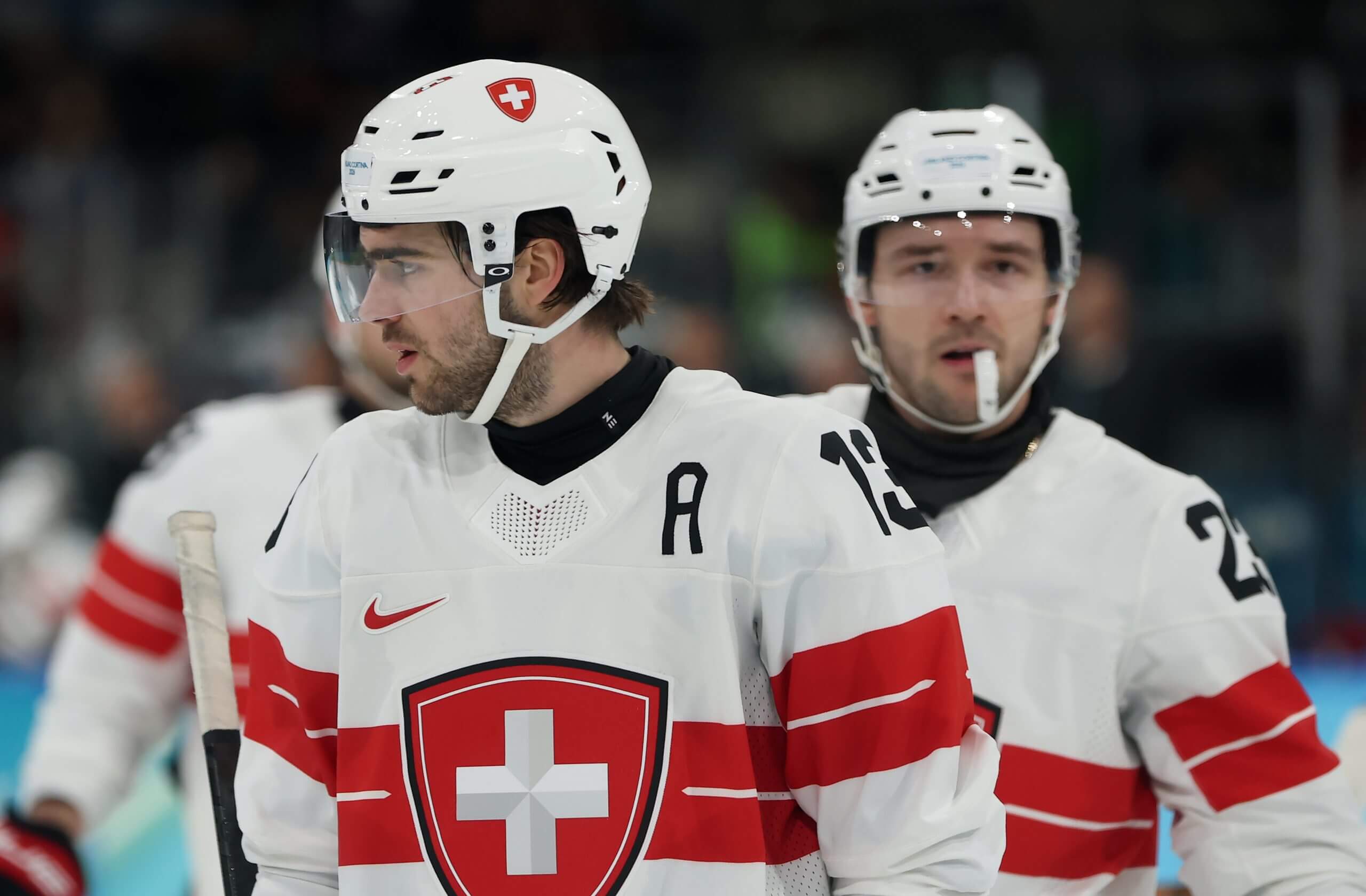 Nico Hischier looks to the side while Switzerland teammate Philipp Kurashev skates behind him.
