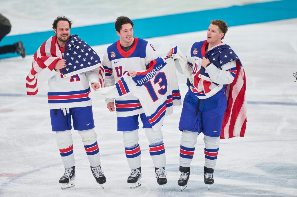 Auston Matthews #34, Zach Werenski #8 and Matthew Tkachuk #19 of Team United States celebrate  the victory and Gold Medal with a jersey of Johnny Gaudreau during the Men`s Ice Hockey final match between USA and Canada on day sixteen of the Milano Cortina 2026 Winter Olympic games at Milano Santagiulia Ice Hockey Arena on February 22, 2026 in Milan, Italy. 