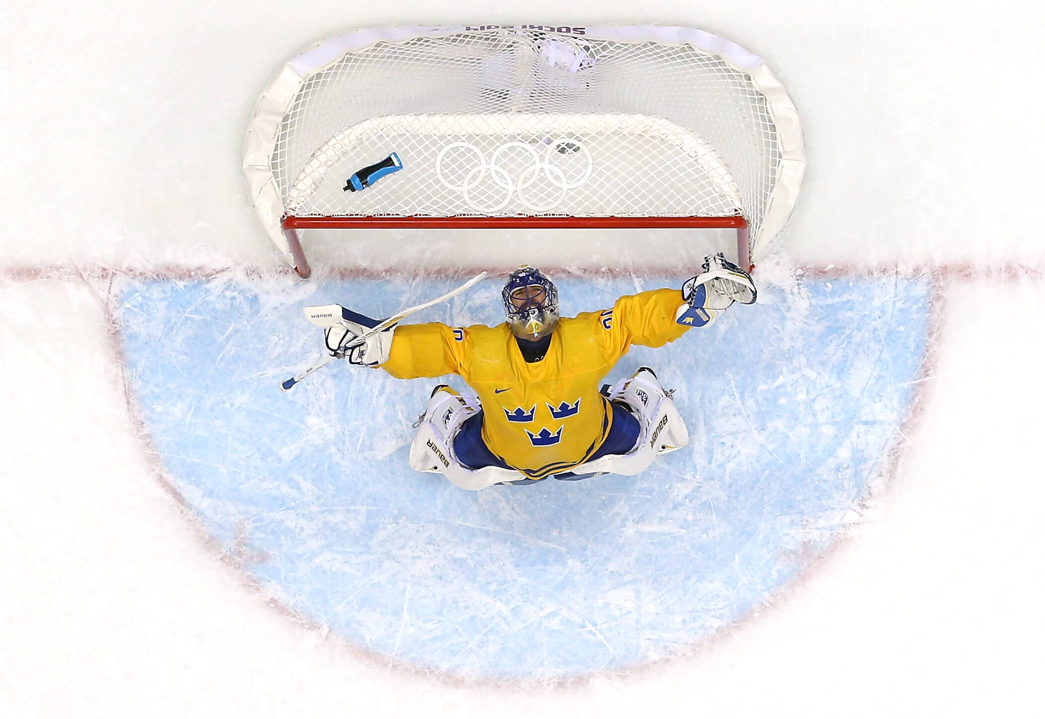 An overhead shot of Sweden's Henrik Lundqvist leaning back arms outstretched in celebration, with an Olympic logo on the net behind him.
