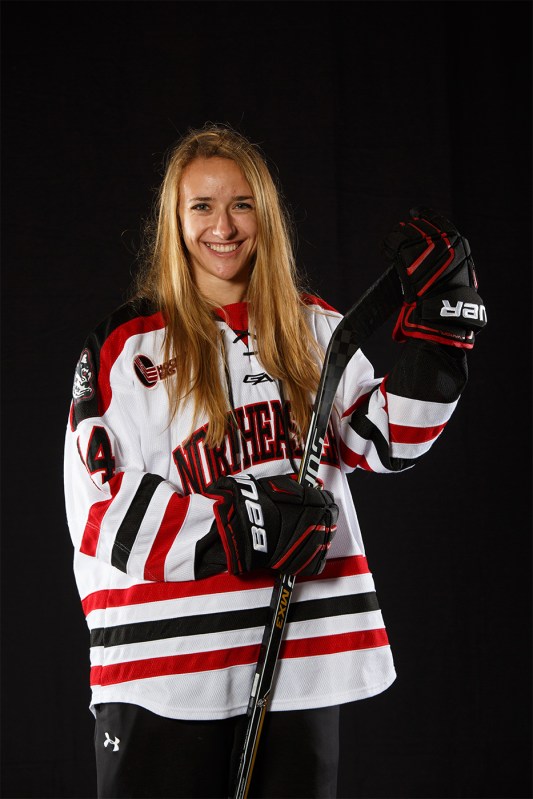 Hayley Scamurra smiles while posing for a photograph in full Northeastern hockey garb.
