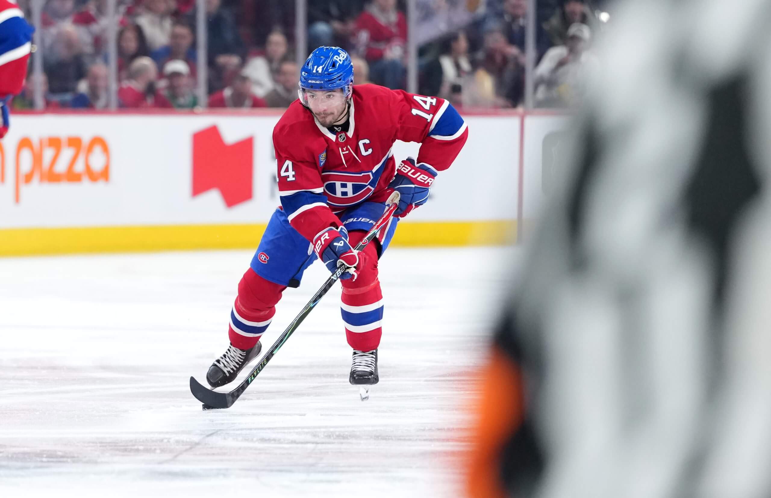 Nick Suzuki skates with the puck, with a referee shoulder partly in the picture.