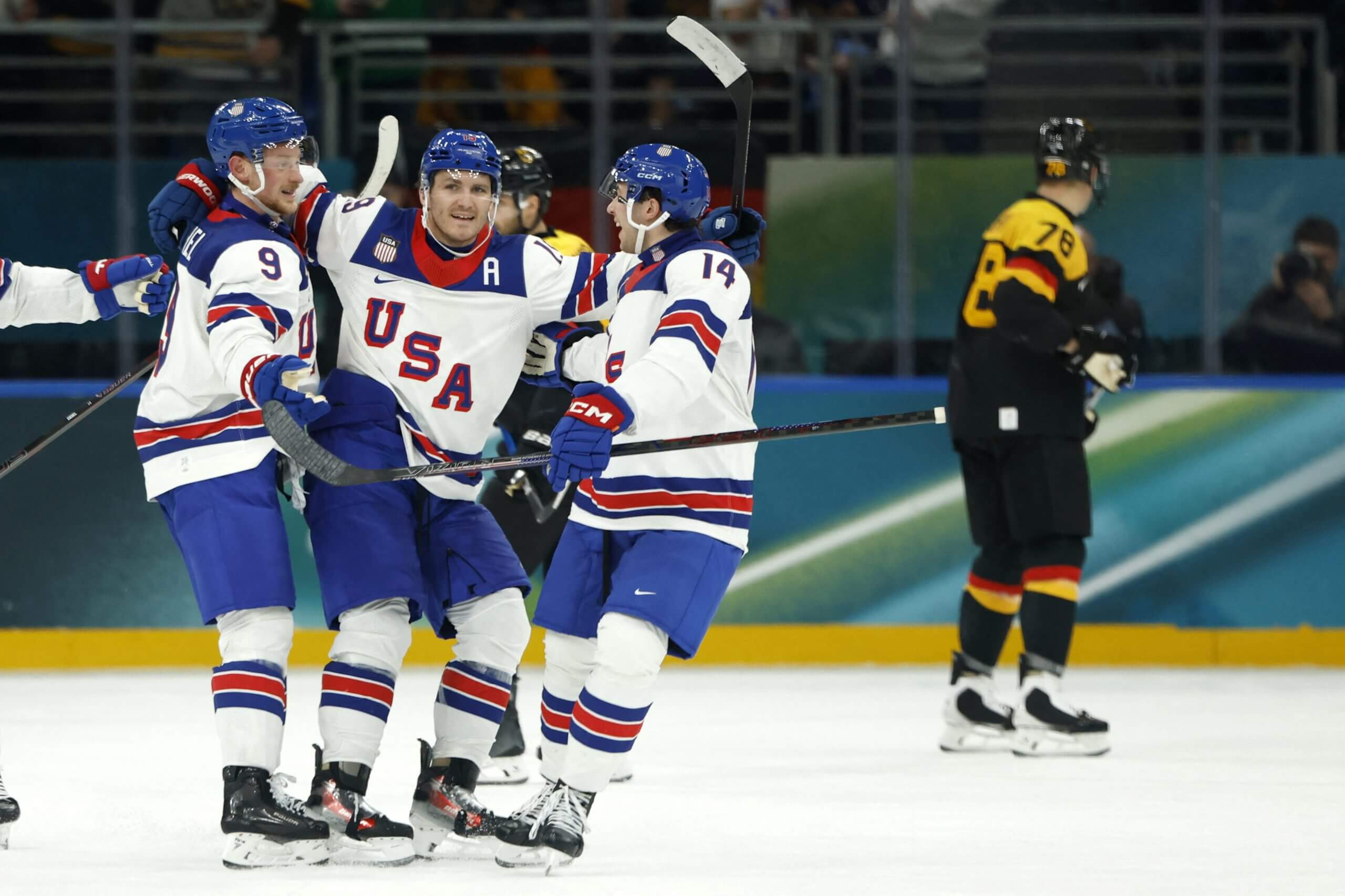 Matthew Tkachuk celebrates with Team USA teammates with a lone German player skating in the distance.