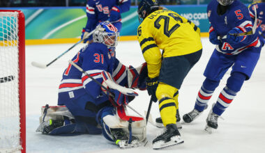 An ice hockey player in a yellow jersey faces the goaltender of Team USA at the 2026 Winter Games.