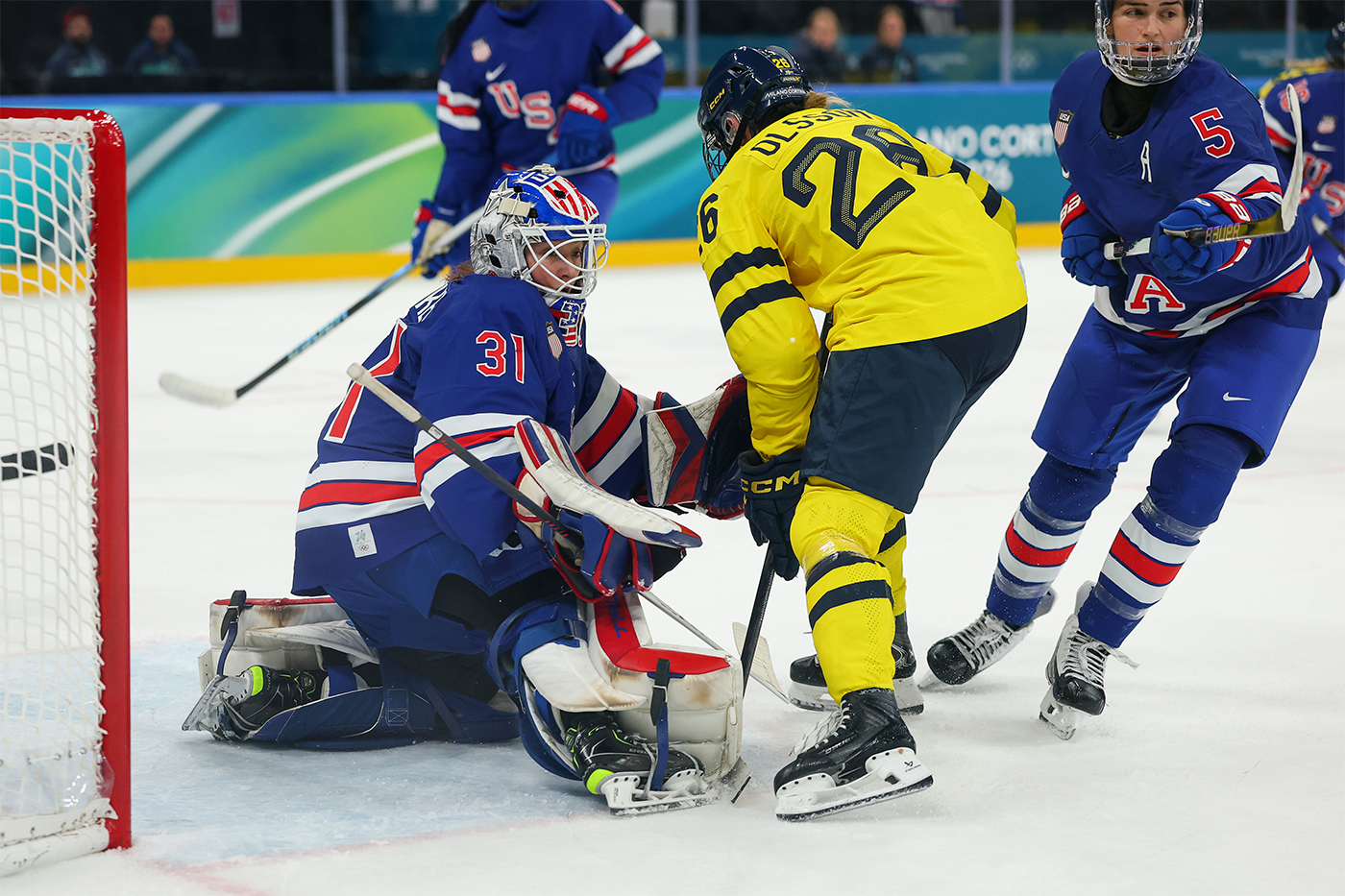 An ice hockey player in a yellow jersey faces the goaltender of Team USA at the 2026 Winter Games.