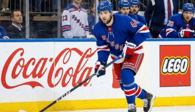NY Rangers defenseman Vladislav Gavrikov (#44), currently the subject of intense trade rumors amid reports he is unhappy with the team's rebuild, skates with the puck past Coca-Cola and LEGO advertisements on the boards.