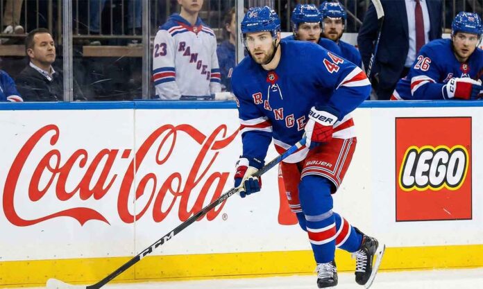 NY Rangers defenseman Vladislav Gavrikov (#44), currently the subject of intense trade rumors amid reports he is unhappy with the team's rebuild, skates with the puck past Coca-Cola and LEGO advertisements on the boards.