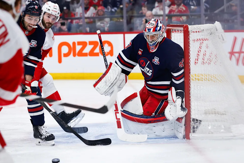 Detroit Red Wings forward J.T. Compher (37) and Winnipeg Jets forward Alex Iafallo (9) with goalie Connor Hellebuyck (37) look for the puck during the first period at Canada Life Centre in Winnipeg, Manitoba, on Saturday, Jan. 24, 2026.