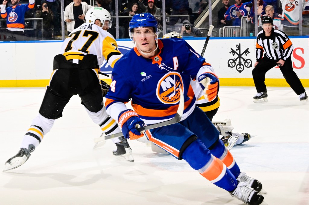 New York Islanders player Bo Horvat (14) celebrates after scoring the game-winning goal in overtime against Pittsburgh Penguins player Erik Gudbranson (17), with a referee and fans in the background.
