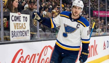 St. Louis Blues captain Brayden Schenn, wearing his white away jersey with the 'C' patch, skates along the boards at T-Mobile Arena, looking towards a female fan behind the glass holding a handmade sign that reads "COME TO VEGAS BRAYDEN!".