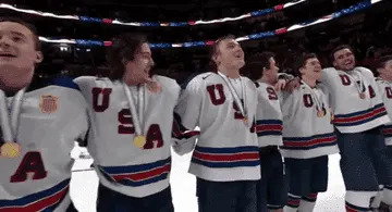 Hockey players wearing USA jerseys and gold medals sway on the ice together, singing