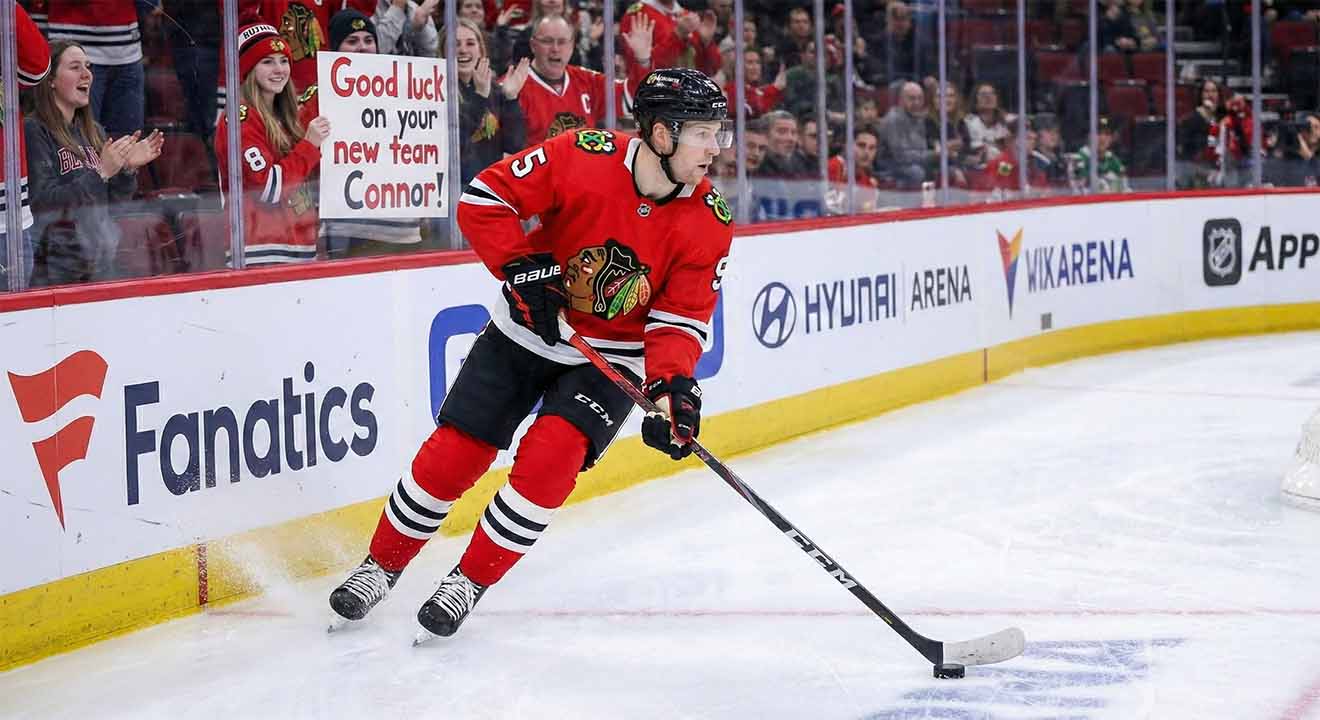 Connor Murphy, Chicago Blackhawks defenseman, skated with the puck during an NHL game with the message "GOOD LUCK ON YOUR NEW TEAM CONNOR!" written on the rink glass, fueling trade rumors to the Dallas Stars and Boston Bruins in 2026.
