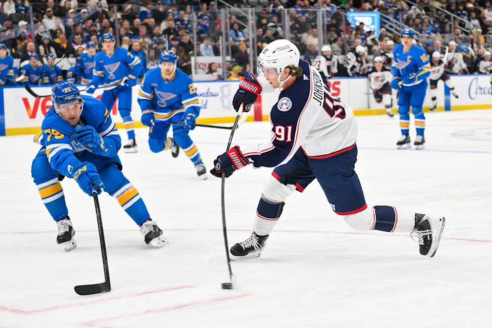 Blue Jackets center Kent Johnson shoots as Blues defenseman Tyler Tucker defends.