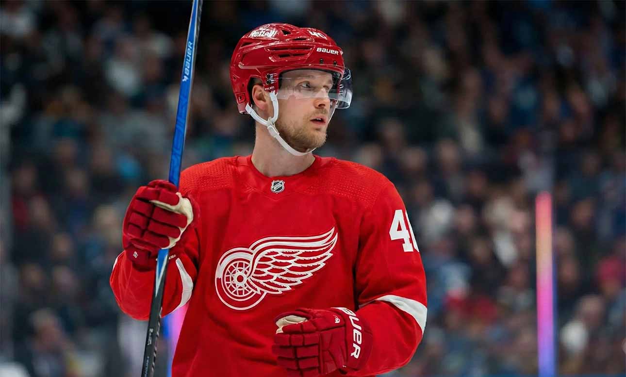 Elias Pettersson, wearing a Detroit Red Wings jersey and helmet, looks towards the right side of the frame while holding a hockey stick on the ice.